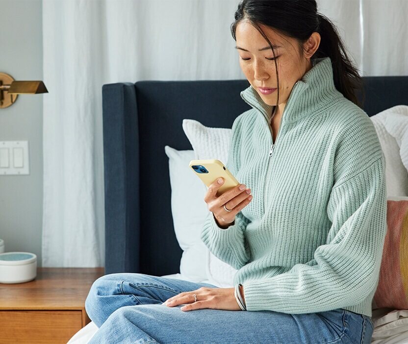 女性はベッドに座って携帯電話を見ながら、記憶に残るパスワードを作成する方法を考えています。