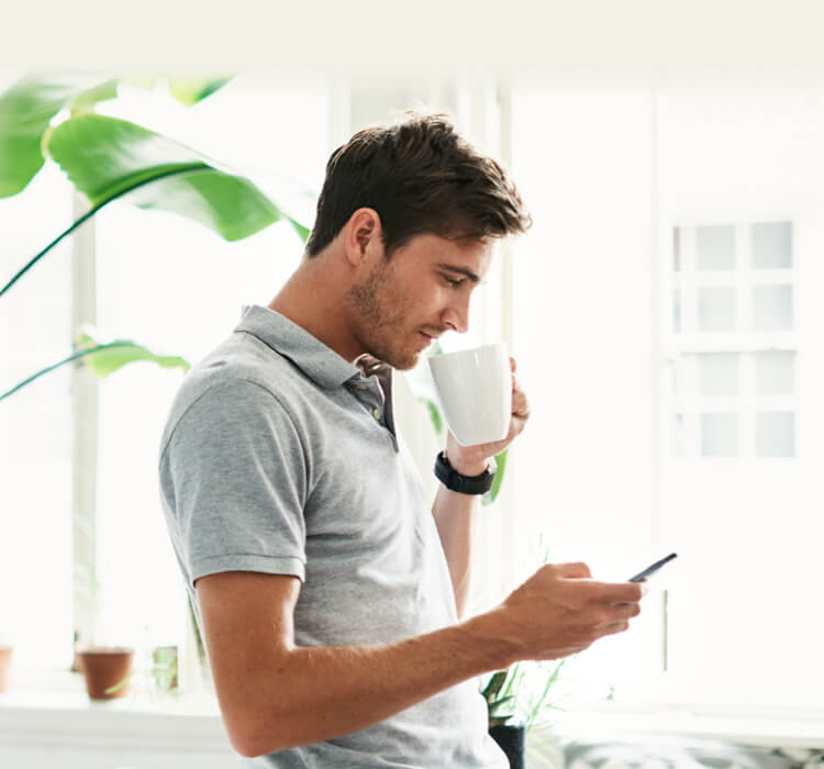 携帯電話を持ちながらコーヒーを飲む男性